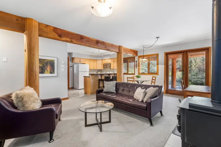 Living area featuring a wood stove, light colored carpet, and beamed ceiling
