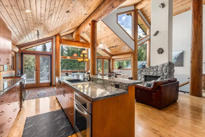 Kitchen featuring light wood-style floors, decorative light fixtures, plenty of natural light, a fireplace, and a wood ceiling with exposed beams