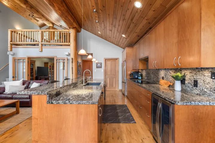 Kitchen with light wood-style floors, a kitchen bar, high vaulted ceiling, brown cabinets, and wine cooler