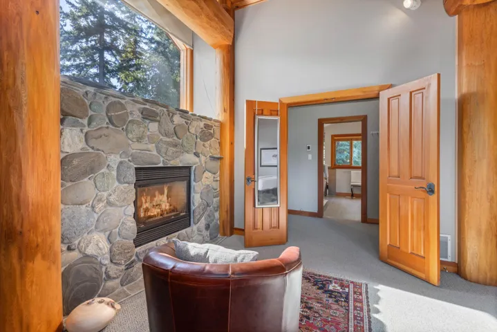 Sitting room with carpet, a stone fireplace, beamed ceiling, and a towering ceiling