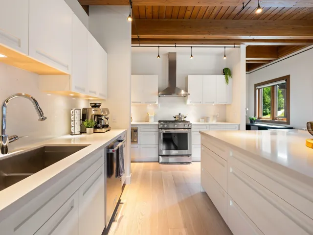 Kitchen featuring appliances with stainless steel finishes, wall chimney exhaust hood, light wood-type flooring, a wooden ceiling with exposed beams, and light countertops