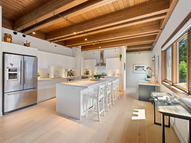 Kitchen with high quality fridge, a wooden ceiling with exposed beams, wall chimney range hood, light wood-style floors, and a kitchen bar