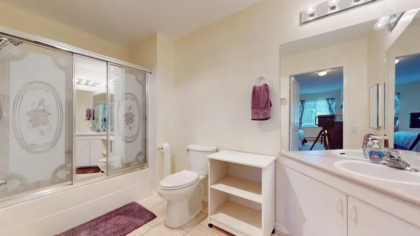 Ensuite with vanity, shower/bathtub combination with glass door, and tile floors