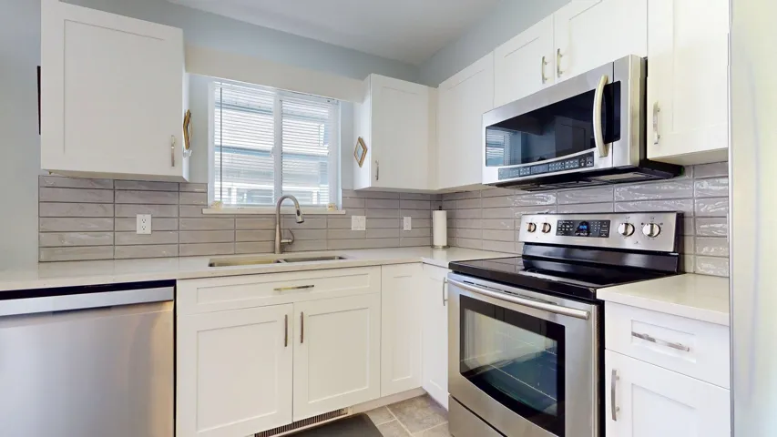 Kitchen with stainless steel appliances, light countertops, white cabinetry, and decorative backsplash