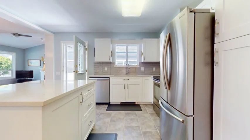 Kitchen featuring appliances with stainless steel finishes, white cabinetry, decorative backsplash, light countertops, and a kitchen island