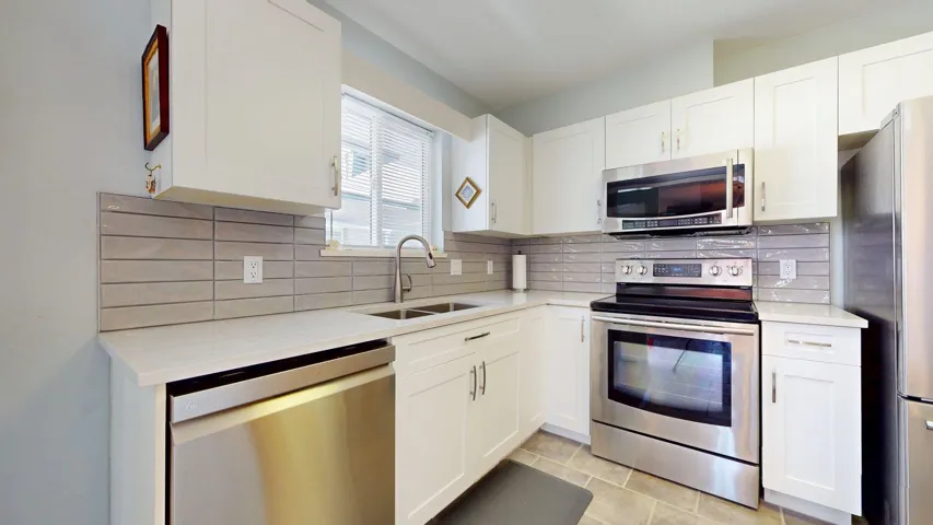 Kitchen featuring appliances with stainless steel finishes, white cabinets, and tasteful backsplash