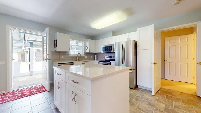 Kitchen featuring stainless steel appliances, white cabinets, a kitchen island, decorative backsplash, and light stone countertops