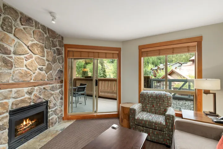 Stone-clad fireplace with a wood mantle and hearth, complemented by a large sliding glass door opening to an outdoor patio with a privacy screen