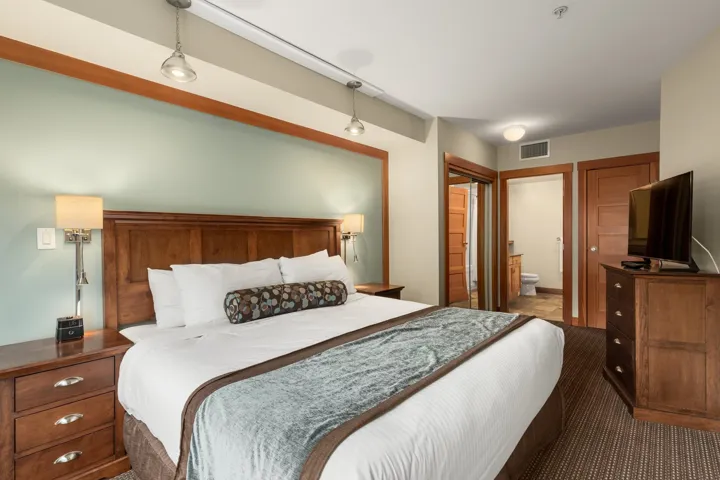 Bedroom featuring a wood headboard, bedside tables with metal hardware, and wall-mounted lighting