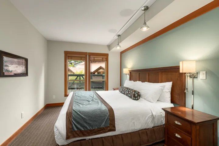 Bedroom featuring two windows with wood trim, track lighting, and a prominent wood headboard