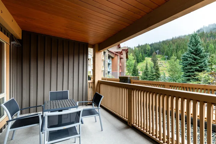 Covered balcony featuring a wood-paneled ceiling, wood railing, and a mountain backdrop with evergreen trees and ski lift infrastructure