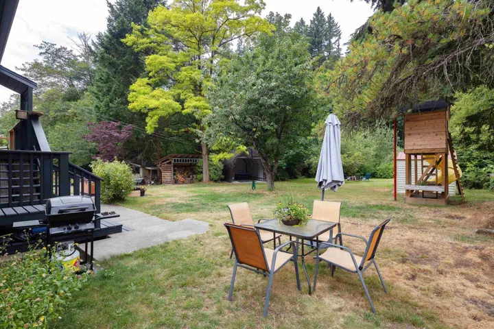View of green lawn with an outbuilding, a patio area, outdoor dining space, and view of scattered trees