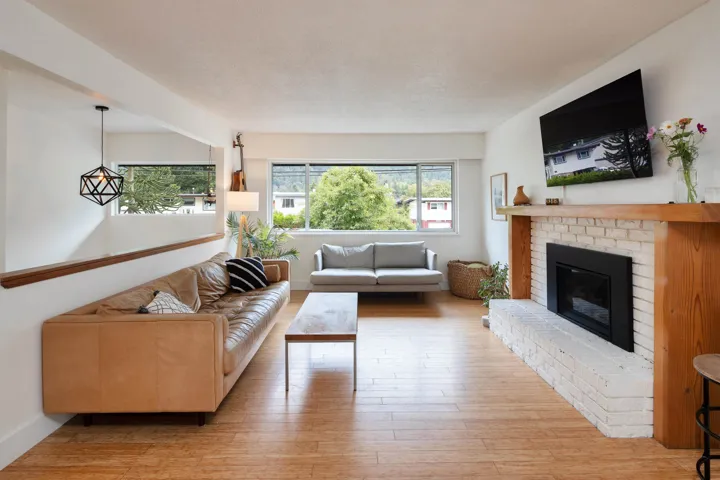 Living room featuring healthy amount of natural light, light wood-style floors, a brick fireplace, and a textured ceiling