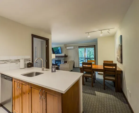 Kitchen featuring brown cabinetry, stainless steel dishwasher, a fireplace, light stone countertops, and rail lighting
