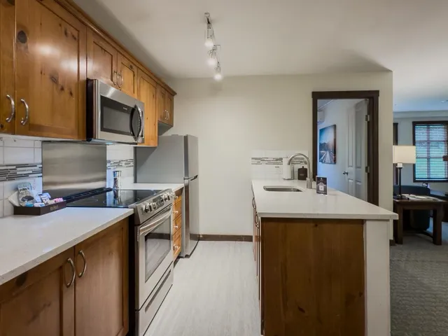 Kitchen featuring tasteful backsplash, stainless steel appliances, brown cabinetry, light stone countertops, and a peninsula