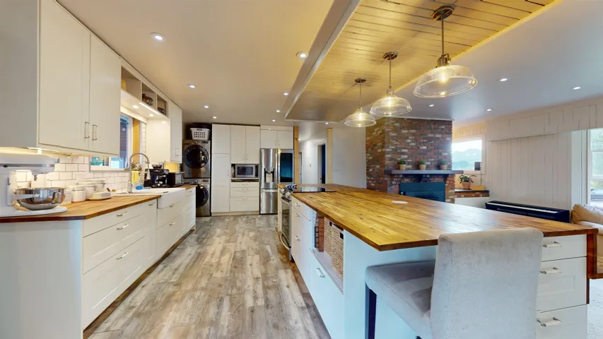 Kitchen with stacked washer / drying machine, a sink, light wood-type flooring, wooden counters, and appliances with stainless steel finishes