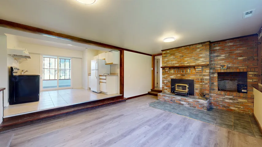 Unfurnished living room featuring a wood stove, visible vents, wood finished floors, and baseboards