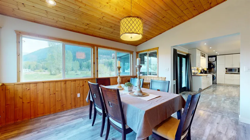 Dining space featuring wooden ceiling, light wood-style flooring, stacked washer / dryer, vaulted ceiling, and wood walls