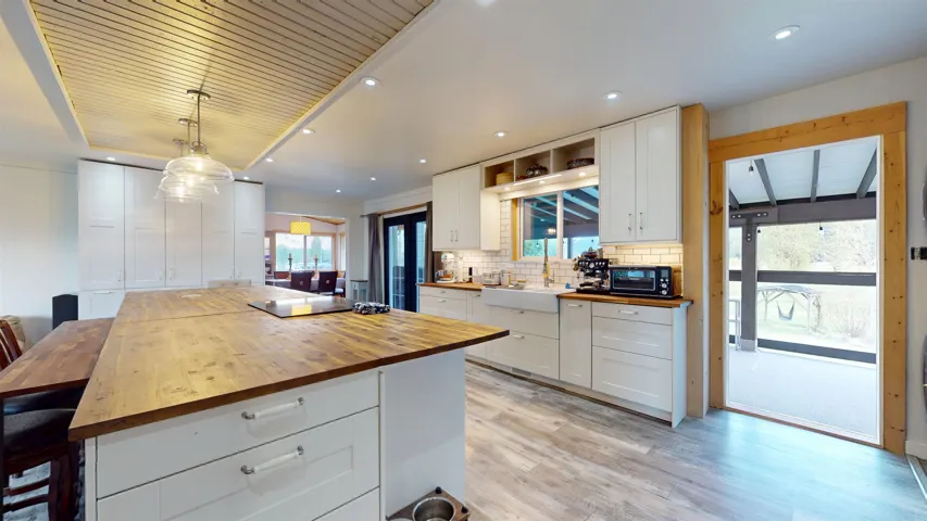 Kitchen with butcher block counters, light wood-style floors, black appliances, a sink, and white cabinetry