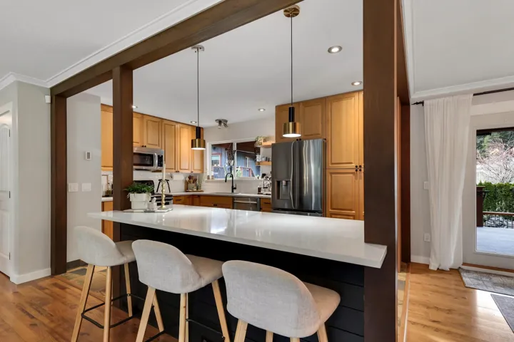 Open-concept kitchen featuring a spacious island with a white solid-surface countertop, warm wood cabinetry, stainless steel appliances, and wood-finish flooring