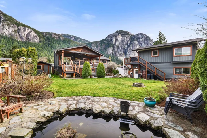 Expansive green lawn with a rock-lined pond, mature trees, and mountainous scenery