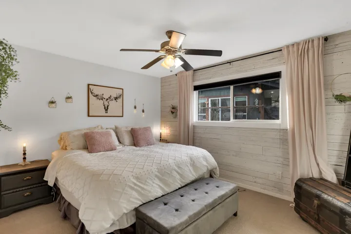 Bedroom featuring a shiplap accent wall, light-colored walls, ceiling fan with integrated lighting, and a large window