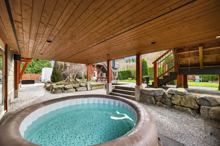 Covered outdoor patio area featuring a built-in hot tub, wood-plank ceiling, recessed lighting, and gravel flooring