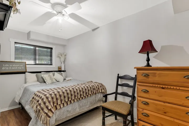 Room featuring wood-finish flooring, a window with black horizontal blinds, and a white ceiling fan