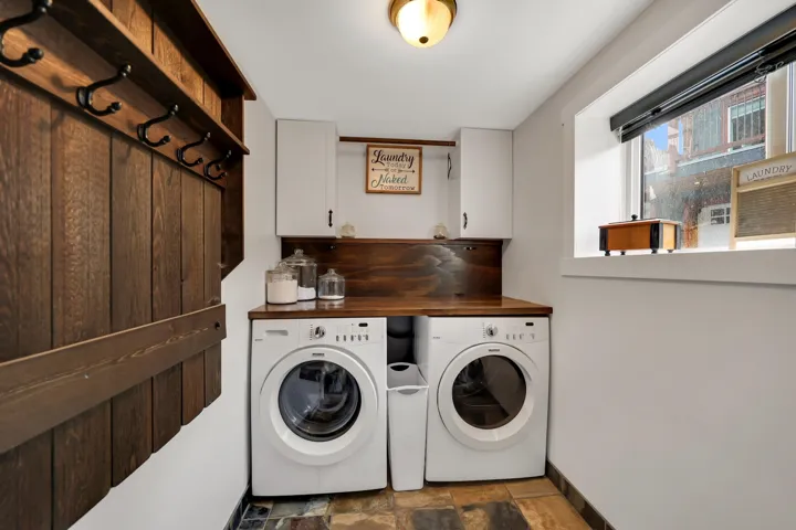 Laundry area featuring a wood-finish countertop, white upper cabinetry, and a wood-paneled wall with hooks