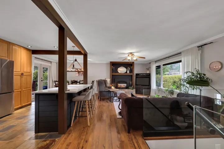 Open-concept living area featuring a kitchen island with seating, wood-finish flooring, a built-in fireplace with shelving, recessed lighting, and large windows