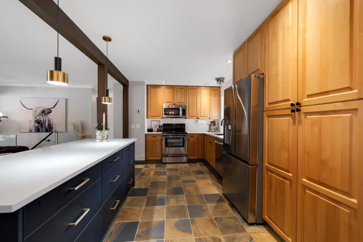 Kitchen featuring a large central island with a white countertop and dark cabinetry, stainless steel appliances, wood-finish cabinetry, and multi-toned tile flooring