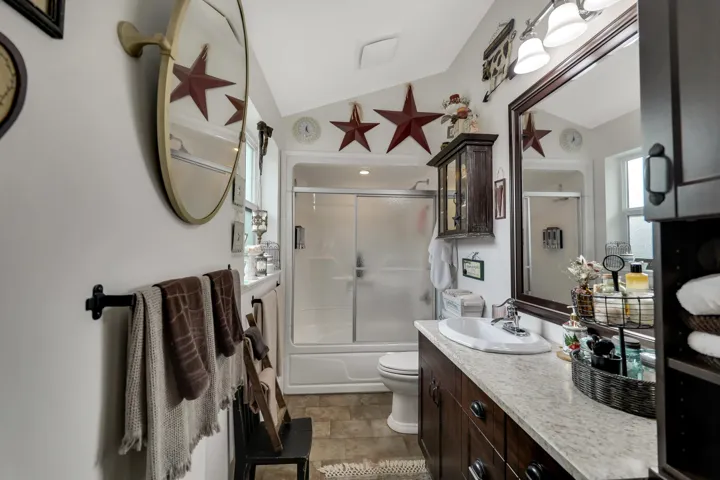 Bathroom featuring a white bathtub with a sliding glass door enclosure, a single vanity with an integrated sink, a light-colored countertop, and dark wood cabinetry