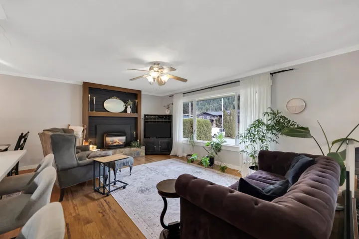 Living area featuring wood-finish flooring, a contemporary ceiling fan, and a fireplace with a stone hearth and wood-paneled surround