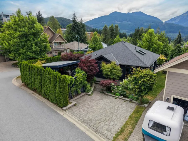 Contemporary home featuring a dark exterior, a paver driveway, an attached carport, and a surrounding privacy hedge