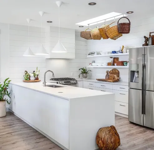 Kitchen featuring a central island with an integrated sink, white shaker-style cabinetry, stainless steel appliances, and wood-finish flooring