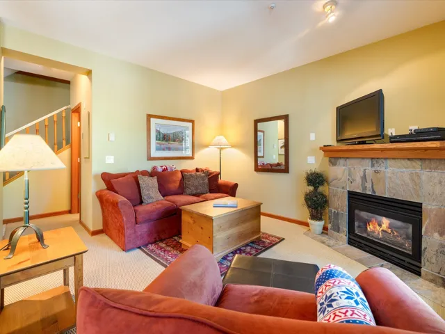 Living area featuring carpet flooring, a stone fireplace, and stairs