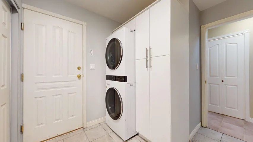 Laundry room with stacked washer / drying machine, cabinet space, light tile patterned flooring, and baseboards