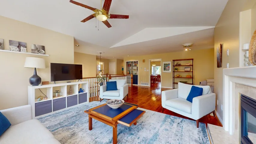 Living room featuring ceiling fan, a high end fireplace, lofted ceiling, wood finished floors, and baseboards