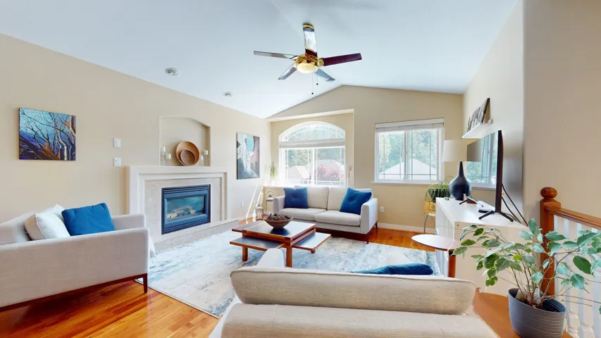 Living room with ceiling fan, wood finished floors, a tiled fireplace, vaulted ceiling, and baseboards