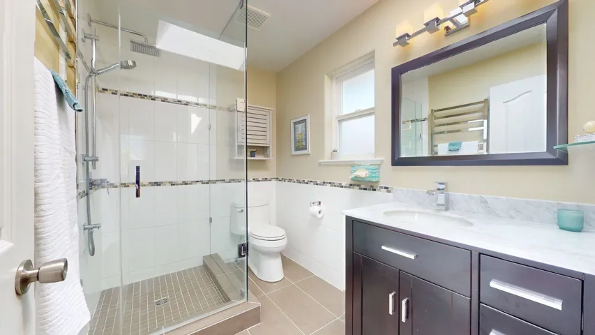 Full bath featuring a stall shower, tile walls, tile patterned flooring, toilet, and vanity