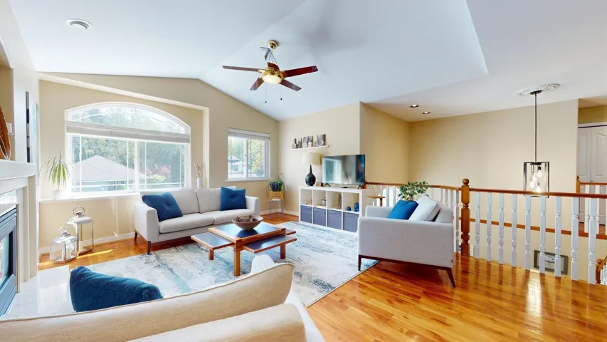 Living area featuring ceiling fan, wood finished floors, a glass covered fireplace, lofted ceiling, and baseboards