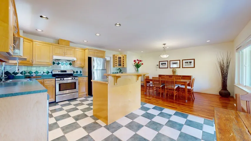 Kitchen with appliances with stainless steel finishes, under cabinet range hood, a sink, a kitchen bar, and light brown cabinetry