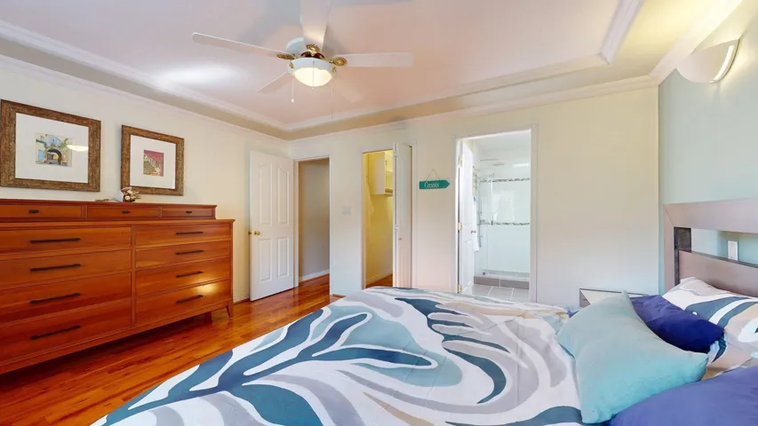 Bedroom with wood finished floors, crown molding, connected bathroom, a ceiling fan, and baseboards