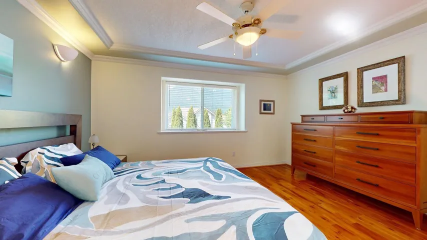 Bedroom featuring light wood-style floors, ornamental molding, a raised ceiling, ceiling fan, and baseboards