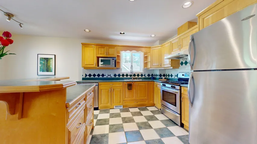 Kitchen with appliances with stainless steel finishes, light floors, a sink, dark countertops, and under cabinet range hood