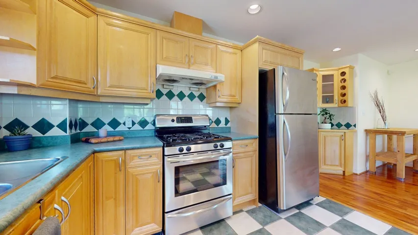 Kitchen with appliances with stainless steel finishes, under cabinet range hood, decorative backsplash, recessed lighting, and light brown cabinets
