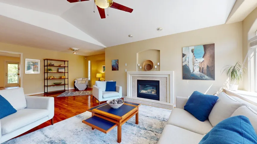 Living room featuring vaulted ceiling, wood finished floors, a ceiling fan, a high end fireplace, and baseboards