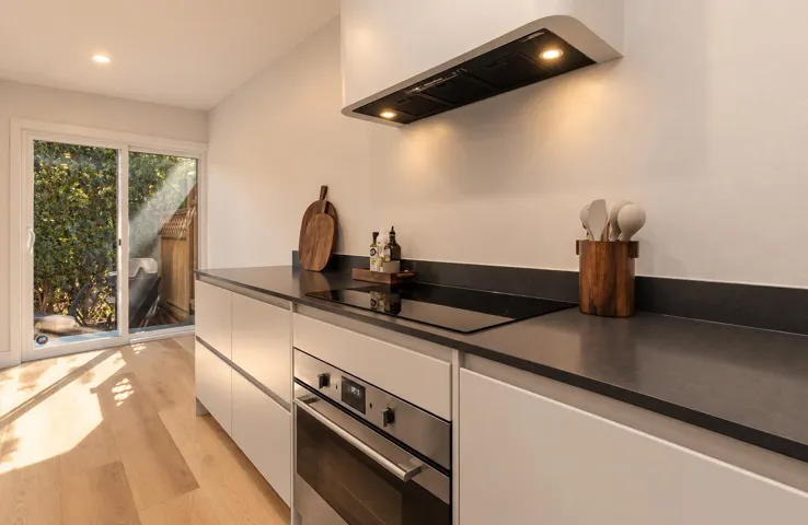 Kitchen featuring flat-panel cabinetry, dark stone countertops, integrated induction cooktop, stainless steel oven, and wood-finish flooring
