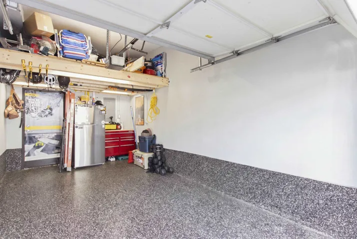Garage interior featuring an epoxy-coated floor, painted walls with a textured wainscot finish, and a ceiling-mounted storage loft