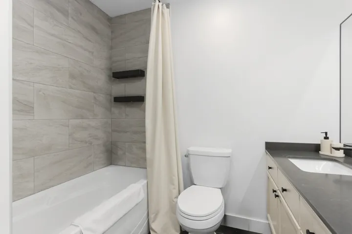 Bathroom featuring a bathtub with full-height stone-finish wall tile, built-in matte black recessed shelving, a vanity with a solid-surface countertop, and an integrated rectangular basin